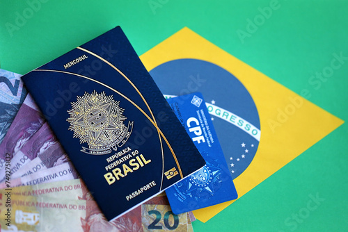 Passport book of Federative Republic of Brazil, CPF taxpayer card and brazilian reais money bills on flag background close up