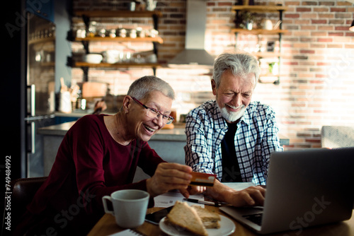 Smiling senior couple using credit card on laptop at home