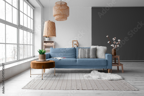 Cozy interior of living room with blue sofa, pouf and and wicker ceiling lamp