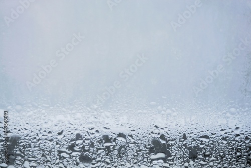 Beschlagene feuchte Glasscheibe mit Wassertropfenmuster vor grau-weißem Hintergrund bei Frost und Kälte am Morgen im Winter