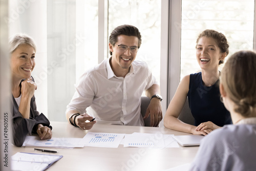 Smiling diverse colleagues gather in boardroom, brainstorm, discuss financial statistics, having fun, joking, laughing cooperating, working together during briefing in office, teamwork, companionship