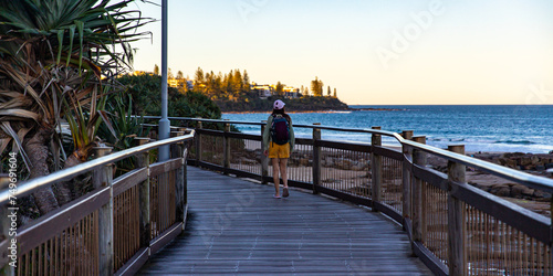 beautiful girl enjoys a sunset at kings beach, caloundra in sunshine coast, queensland, australia; wooden boardwalk above the ocean