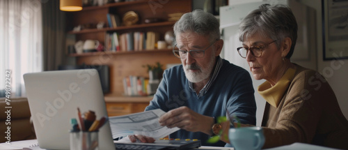 Mature couple concentrating on finances with paperwork and laptop at home.