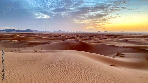 Landscape of Erg Admer in the Sahara desert, Algeria. Waves of dunes at sunrise with, in the distance, the rock formations of Tassilis