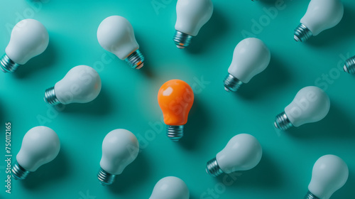 An orange lightbulb glowing among a group of white lightbulbs on a teal background, representing a unique idea or solution.