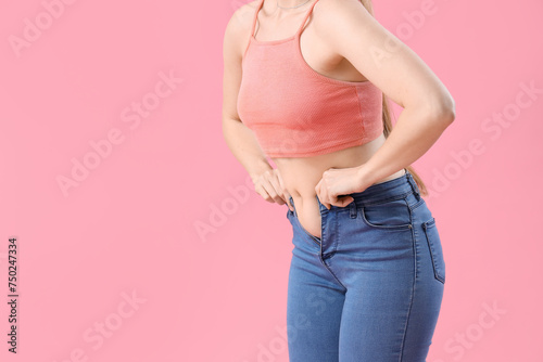 Young woman in tight jeans on pink background, closeup. Weight gain concept