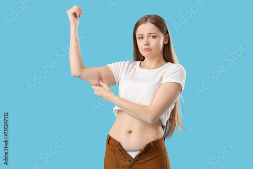 Young woman in tight pants with chubby arms on blue background. Weight gain concept