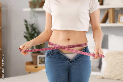 Young woman in tight jeans measuring her belly at home, closeup. Weight gain concept