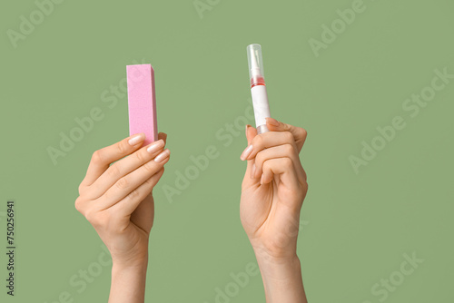 Female hands with cuticle oil pen and nail buffer on green background