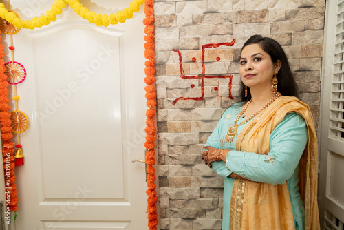 Happy young indian woman standing in her new house with swastik red color in background wall. Griha Pravesh Concept