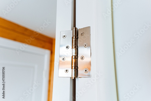 Close up of a hardwood door hinge on a white door with wood stain and varnish