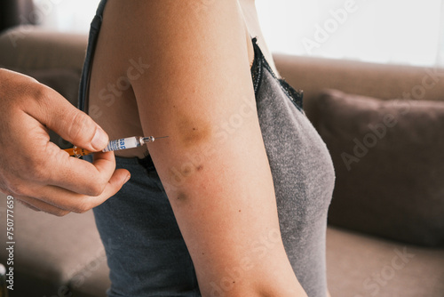 Closeup of giving an intramuscular anticoagulant injection into the arm using a safety syringe. Blood thinning medication or insulin injection. Bruising on the arm caused by previous injections