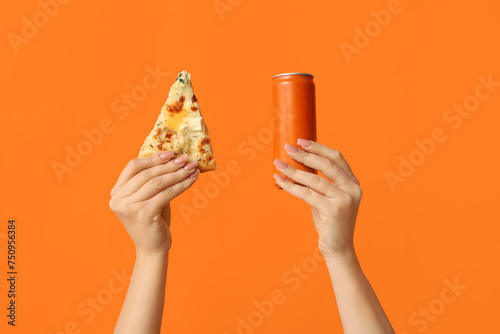Female hands holding tasty pizza slice and can of soda on orange background
