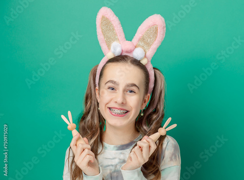 Girl with joyful smile, wearing glittery pink bunny ears holding wooden bunny figures, showcases her braces