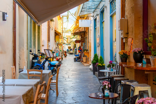 A narrow alley full of sidewalk cafes and shops in the historic old town of Aegina, Greece, on the island of Aegina, one of the Greek islands in the Saronic Gulf.