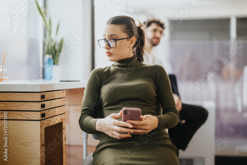 Woman working on her phone while being interrupted by a colleague. She is carefully listening to him.