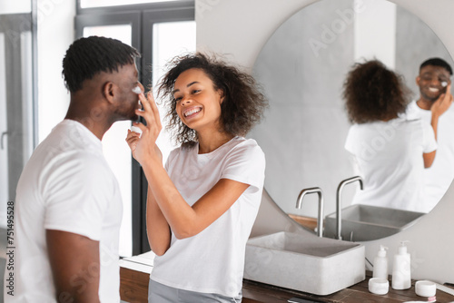 Young black couple shares flirty moment moisturizing skin in bathroom
