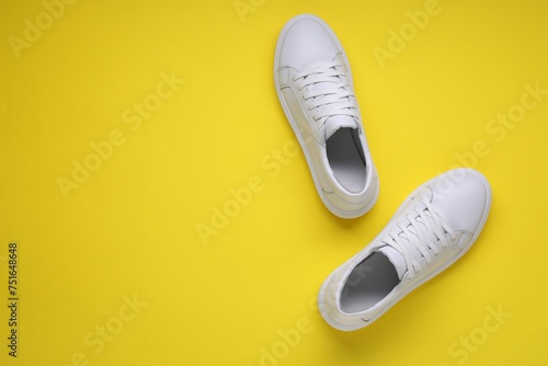 Pair of stylish white sneakers on yellow background, top view. Space for text