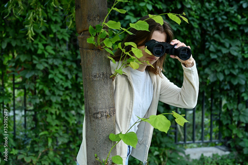 Close-up of a young woman watching someone with binoculars while hiding