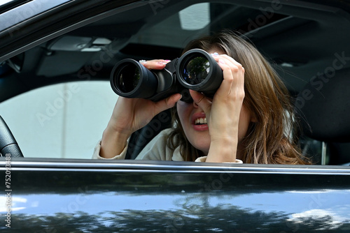A young woman funny spying on someone through binoculars from a car
