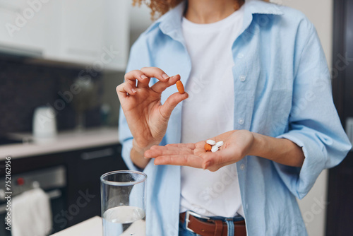 Woman holding pill standing in front of glass water preparing take medication healthcare concept