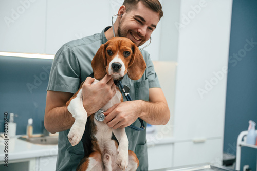 Positive man is holding animal. Dog in veterinarian clinic with male doctor