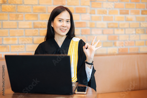 Asian female lawyer gives thumbs up OK Using a laptop to type in a law office from police investigations and judgments from judges to prosecute clients against defendants who have committed crimes.