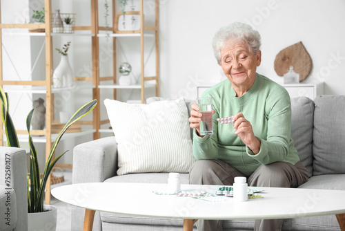 Senior woman with glass of water and pills at home