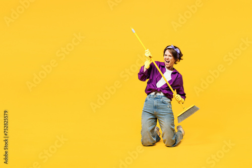 Full body young woman wears purple shirt casual clothes do housework tidy up hold in hand brush broom pov play guitar kneeling isolated on plain yellow background studio portrait Housekeeping concept