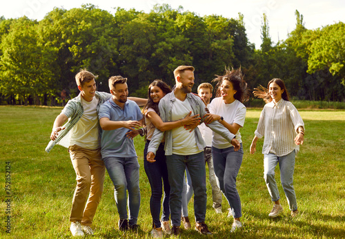 Portrait of a group of happy laughing people friends hugging in the summer park and smiling. Young smiling students having fun in nature outdoors. Friendship and togetherness concept.