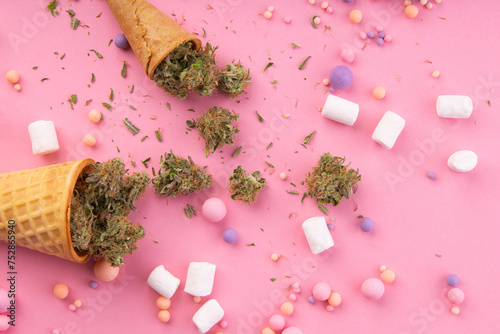 Dry buds of medical marijuana lie on waffle ice cream cones on a pink background. There are candies and marshmallows . around. Alternative medical cannabis treatment