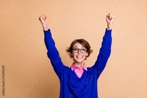 Photo of delighted positive person toothy smile raise fists attainment empty space isolated on beige color background