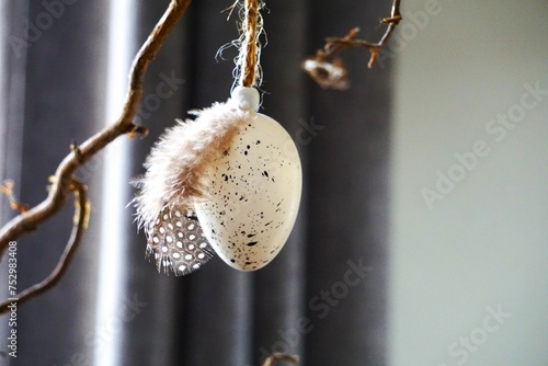Przystrojone białe jajko na Boże Narodzenie. Ozdoba świąteczna w postaci jajka przyozdobionego małym piórem od perliczki. 