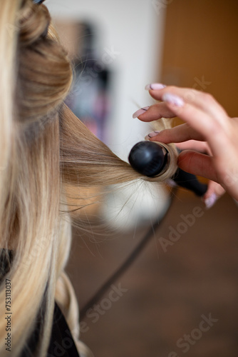 women hairdresser makes the models blonde hair with black curling iron