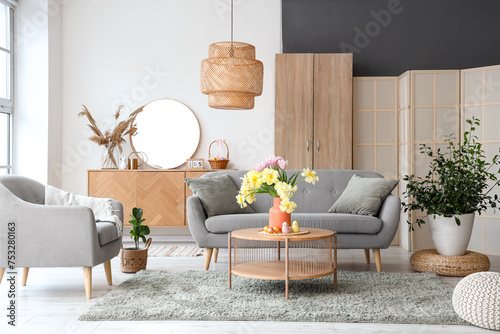 Interior of modern living room with flowers, Easter eggs and porcelain quails on coffee table