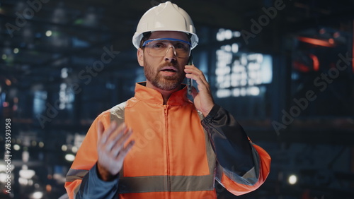 Professional craftsman talking cellphone at factory warehouse in uniform closeup