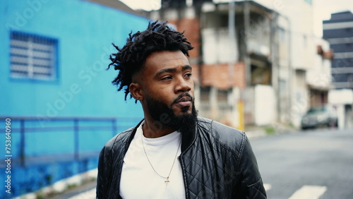 One contemplative young black man walking in street feeling preoccupied and ruminating thoughts while on urban stroll, tracking shot close-up face in motion