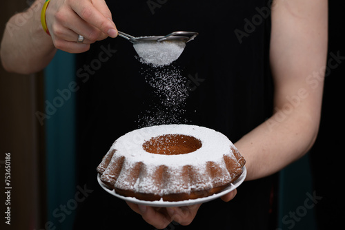 Ciasto cytrynowe w formie babki z dziurką w trakcie posypywania cukrem pudrem z bliska
