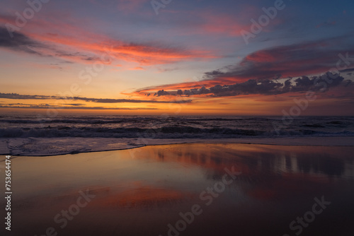 Sunset landscape of a beautiful and paradisaical beach with the clouds reflected on the water. Summer and vacations concept background.