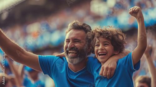 An excited father and son in blue shirts cheer for their favorite team during a football match. Football concept