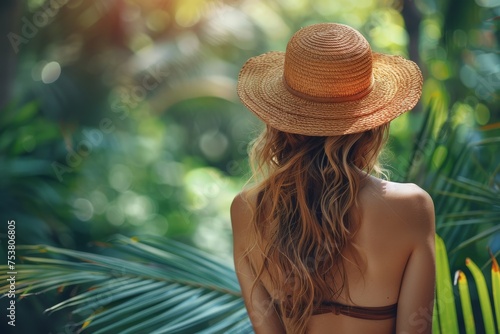 A woman in a straw hat gazes at a lush tropical landscape, her bare back suggesting a connection to nature and leisure