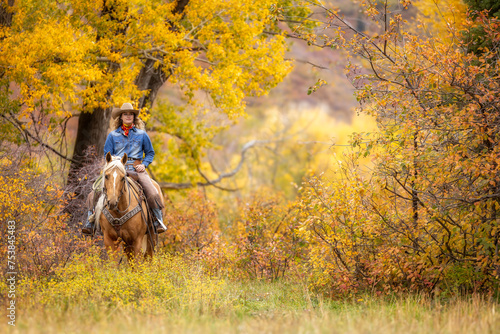 Colorado Cowgirl with a palomino horse and her herding dog in the mountains with colorful aspens in the background