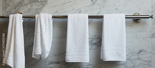 Several white towels are neatly hung on stainless steel hooks attached to the marble walls of a modern bathroom.