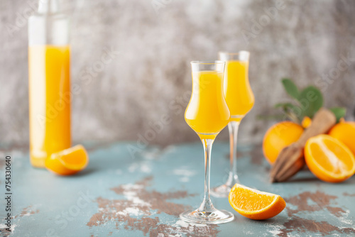 Arancello in grappas wineglass, sweet Italian orange liqueur, traditional strong alcoholic drink and oranges on the light blue wooden background.