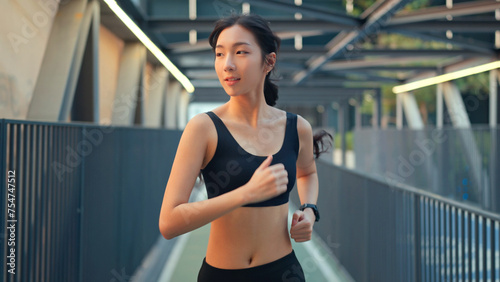 Young asian woman runner is training in the summer sunset within a city, The athlete fit and firm girl exercising by jogging workout sport outdoor for her healthy wellness.