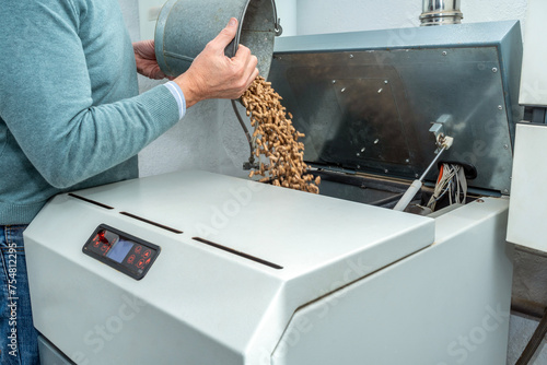 Man filling a biomass boiler or stove with wood pellets. Biofuel heating system at home.