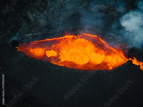 Flowing lava, hot magma spilling out of the volcano crater, aerial side view. Concepts of volcanic eruption and Icelandic land of fire and ice.