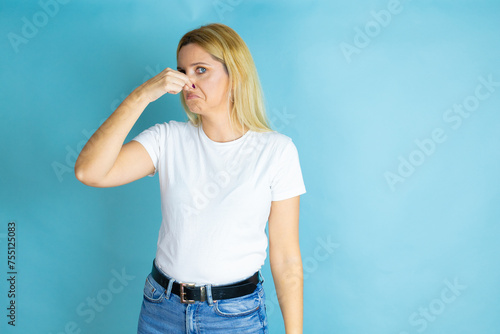Young beautiful woman wearing casual t-shirt over isolated blue background smelling something stinky and disgusting, intolerable smell, holding breath with fingers on nose