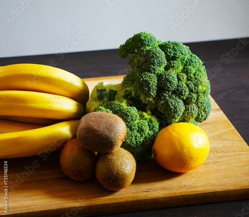 Świeże owoce i warzywa poukładane na desce do krojenia. Zdrowa dieta dla wegetarian. Ekologiczne owoce i warzywa leżą na stole. Brokuł, kiwi, banany i cytryna.