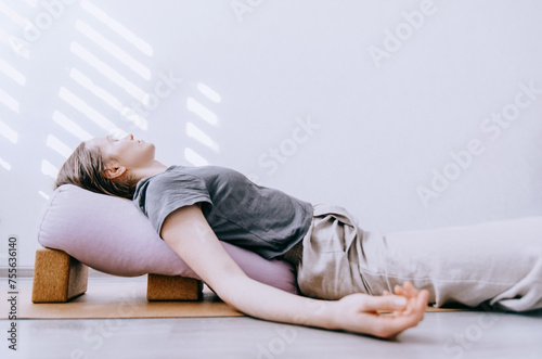 Woman in casual clothing doing yin/restorative yoga with bolster supported by blocks